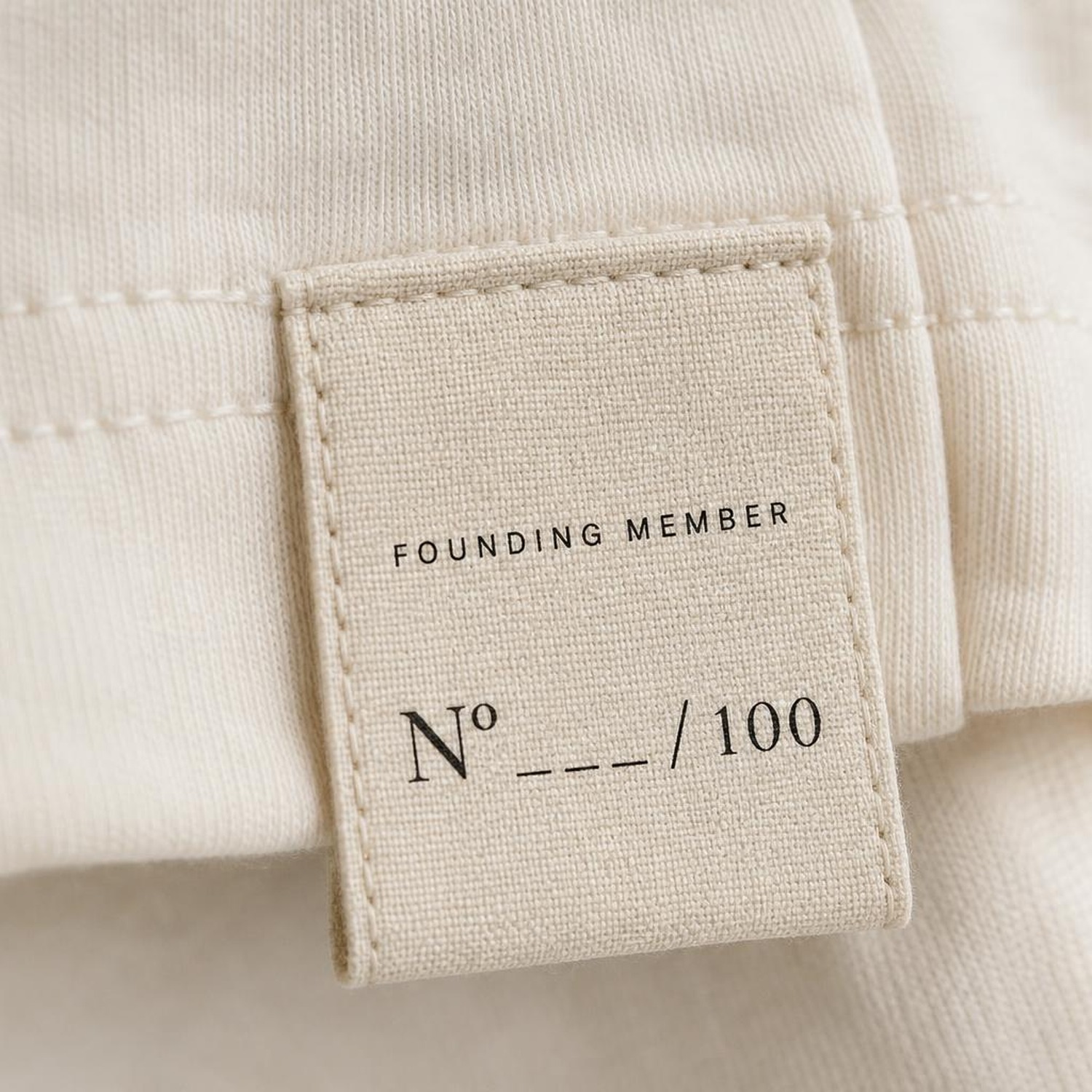 Woven Founding Member hem label reading Nº ___ / 100 on the ivory tee